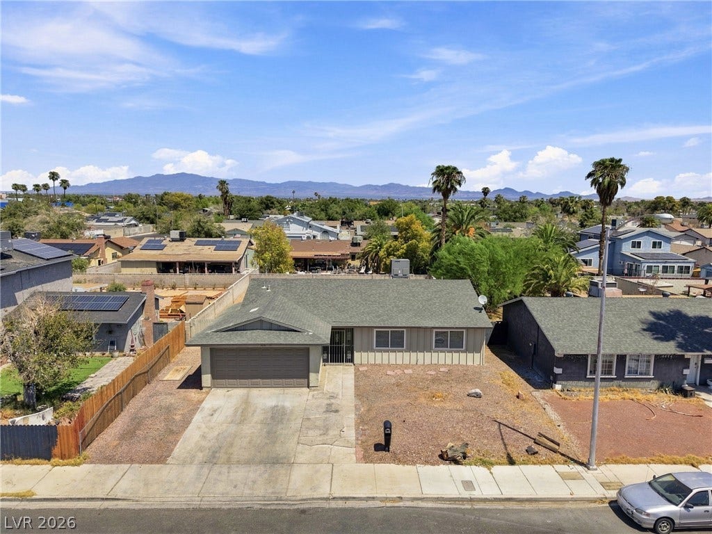 An elevated street view showcases the front facade, concrete driveway, and distant mountain silhouettes.