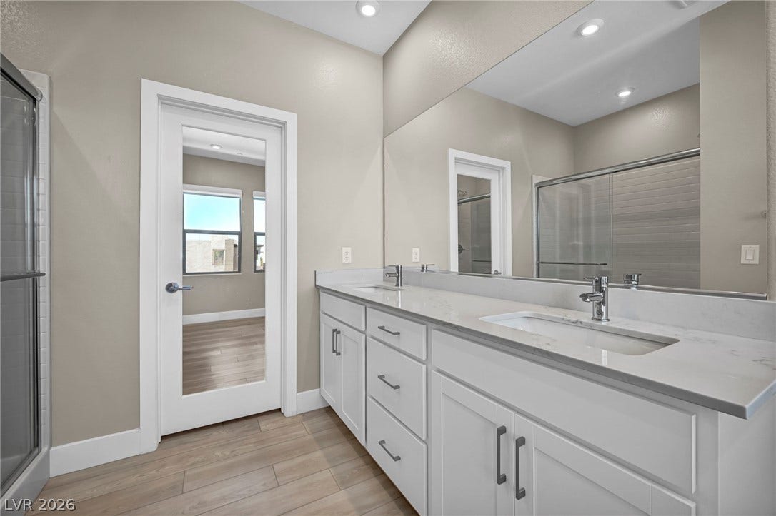 9826 Canyon Sage Street, Las Vegas, NV 89141 Double vanities with stone counters and a mirrored door accent this modern bathroom.
