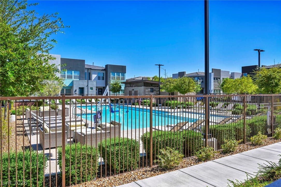 9826 Canyon Sage Street, Las Vegas, NV 89141 A secured community swimming pool sits adjacent to modern residential buildings under clear blue skies.