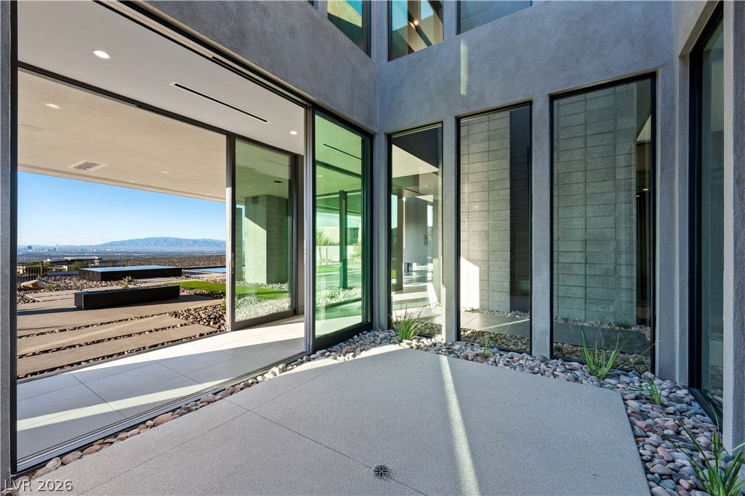 25 Boulderback Drive, Henderson, NV 89012 Towering floor-to-ceiling glass doors open to connect a modern courtyard with expansive mountain views.