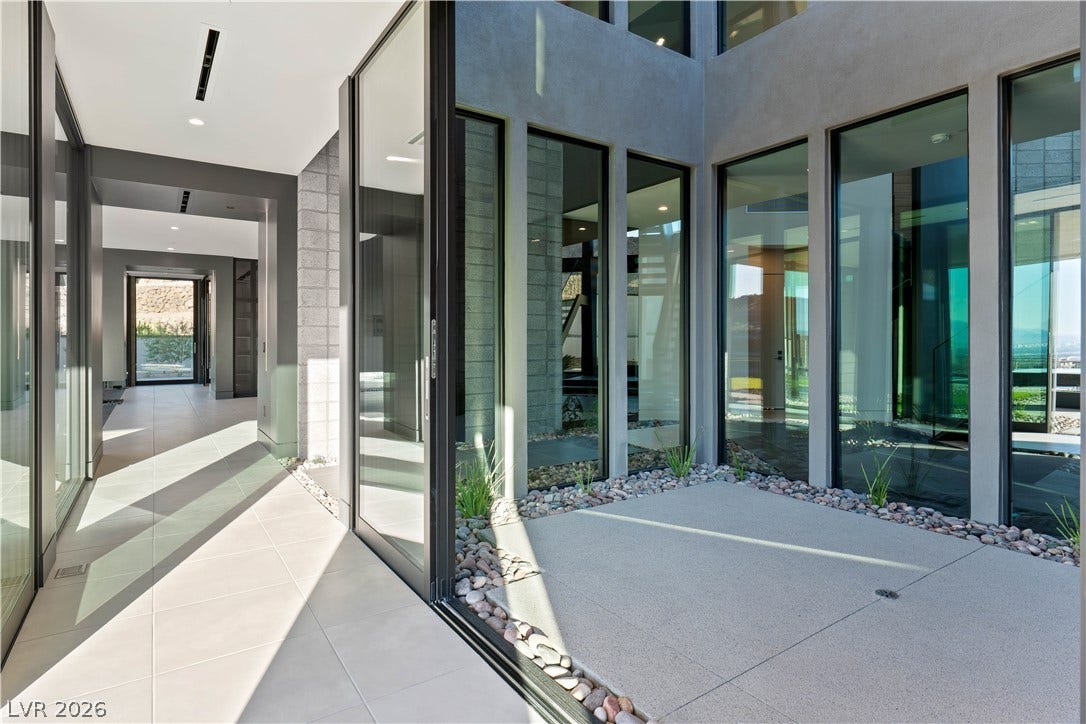 25 Boulderback Drive, Henderson, NV 89012 Floor-to-ceiling glass doors open seamlessly from a tiled corridor onto a concrete courtyard.