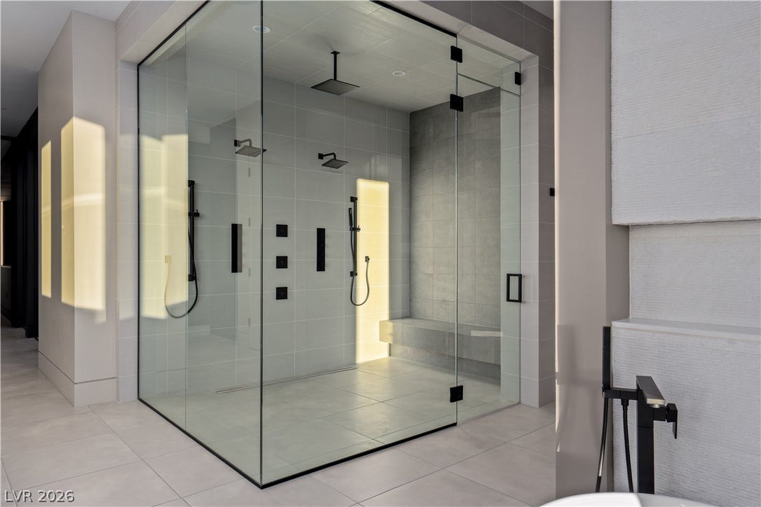 25 Boulderback Drive, Henderson, NV 89012 An oversized glass-enclosed walk-in shower features built-in tile seating and modern black fixtures.