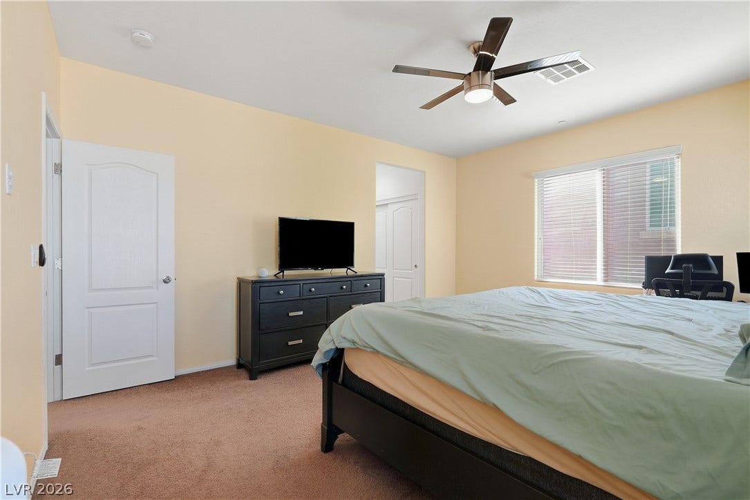 Plush carpeting and wide windows define this comfortable bedroom space.