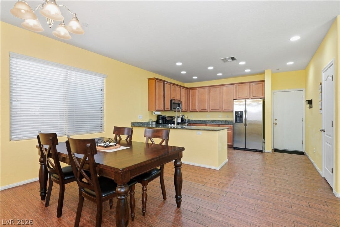 An open kitchen and dining area features tile flooring, recessed lighting, and wooden cabinetry.