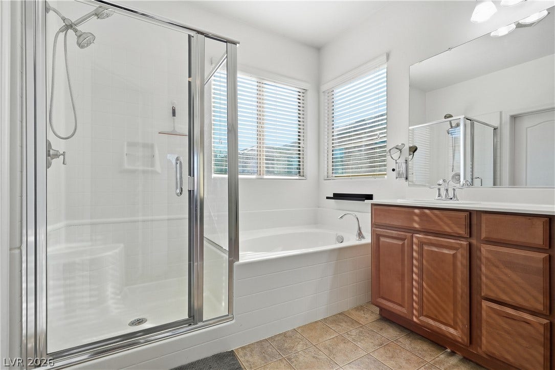 Natural light from dual windows illuminates the tile flooring, soaking tub, and walk-in shower.