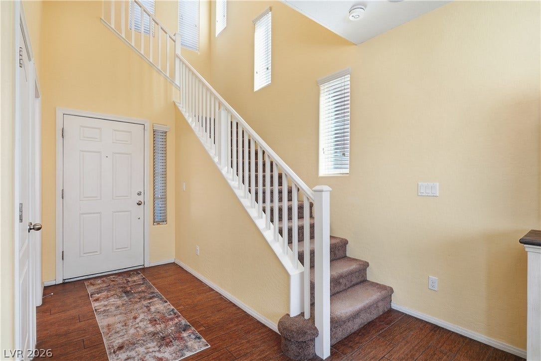 A spacious entrance foyer showcases a carpeted staircase alongside rich wood floors and high ceilings.