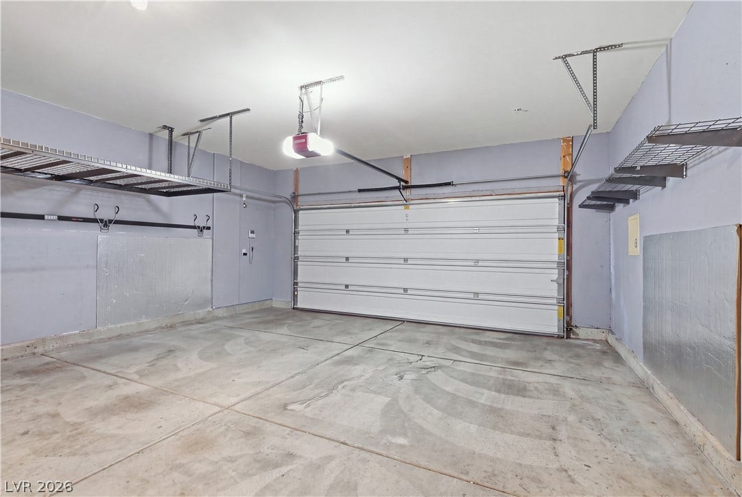 A spacious garage features durable concrete flooring and overhead storage racks.