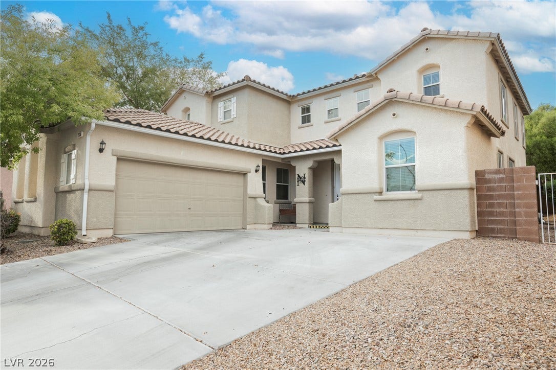 An expansive concrete driveway leads to the attached two-car garage of this multi-level stucco home.