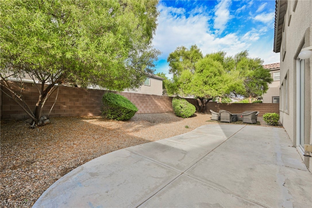 An expansive concrete patio overlooks the low-maintenance gravel yard enclosed by a block wall.