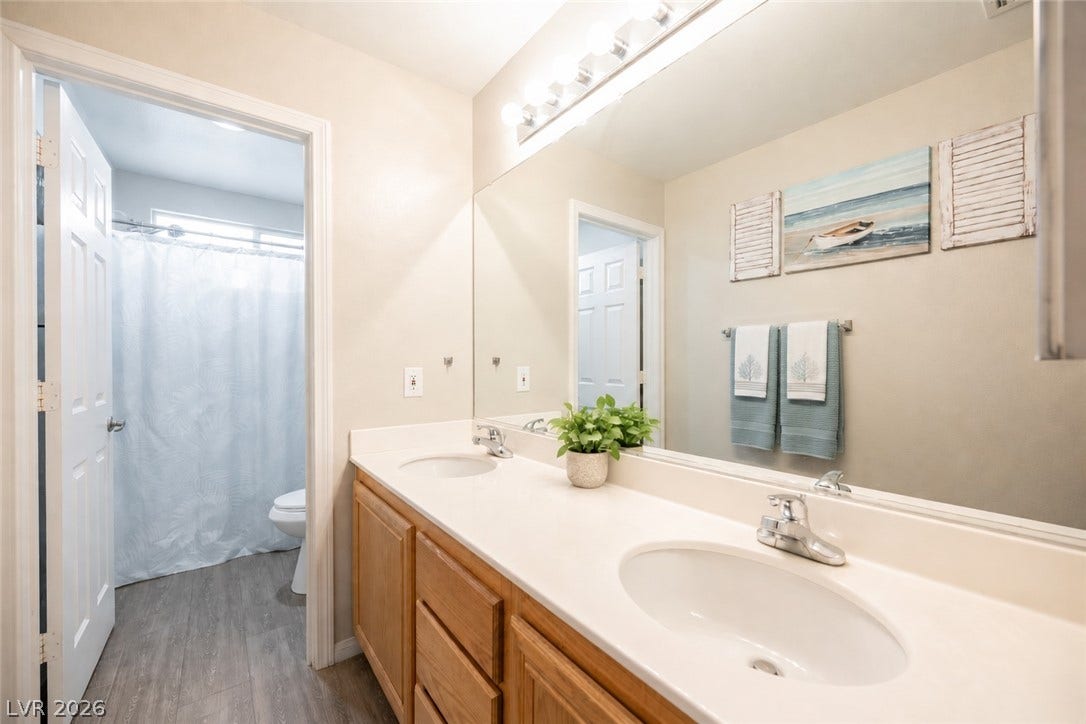 A long double vanity with wood cabinetry sits beneath an expansive mirror.