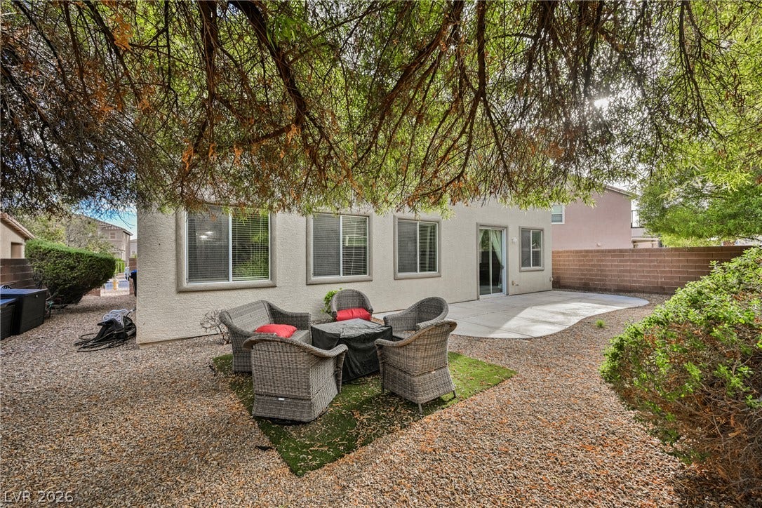 Mature trees shade a gravel yard featuring a concrete patio and stucco exterior.