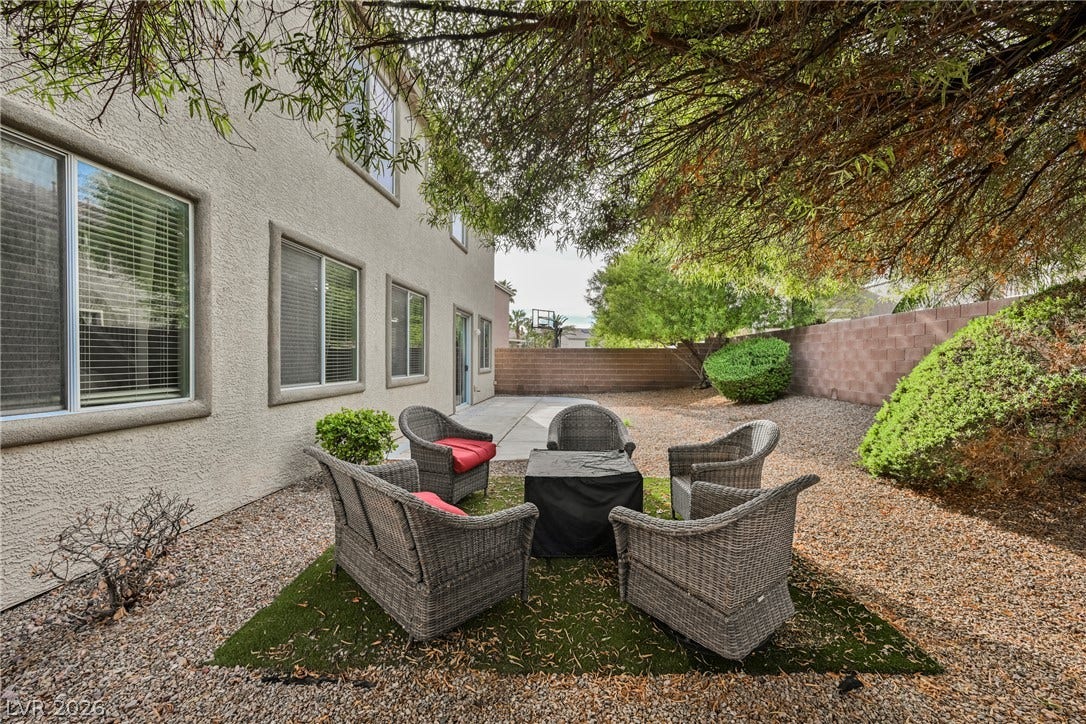 Mature trees shade a gravel courtyard along the side of the stucco home.