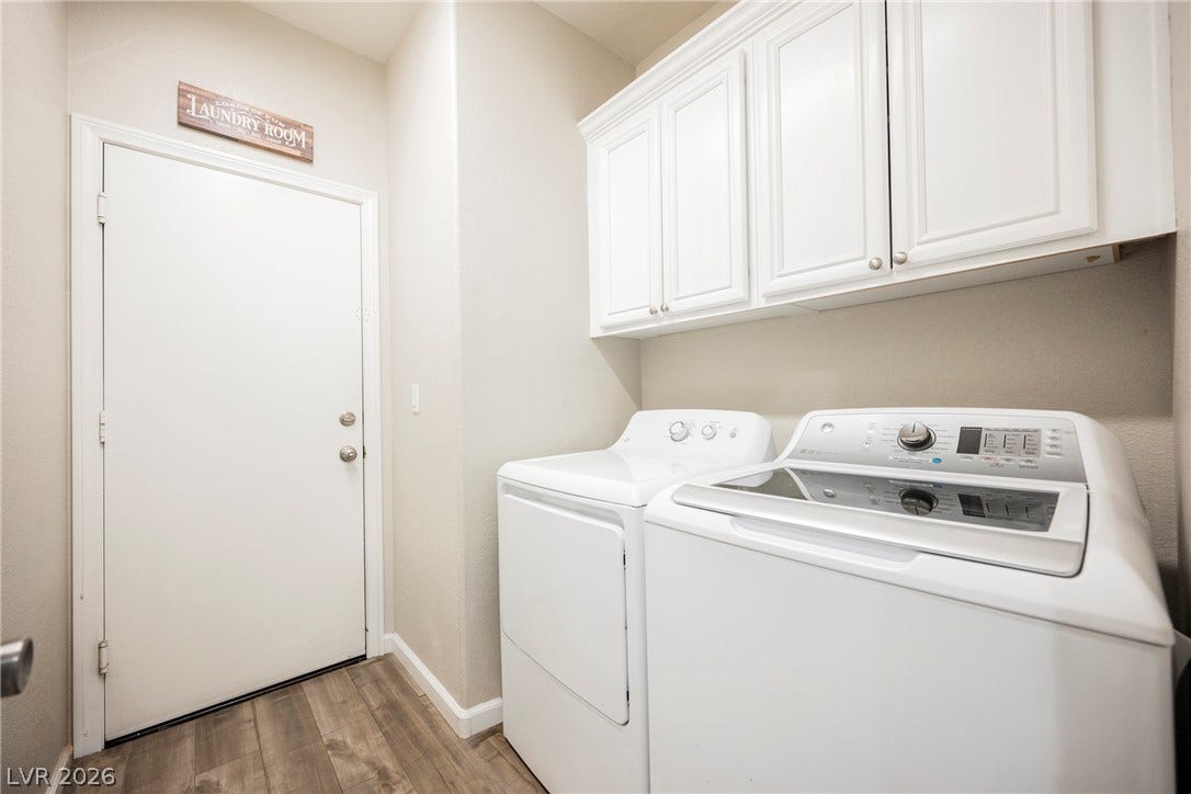A functional laundry area features overhead cabinetry and durable wood-look flooring.