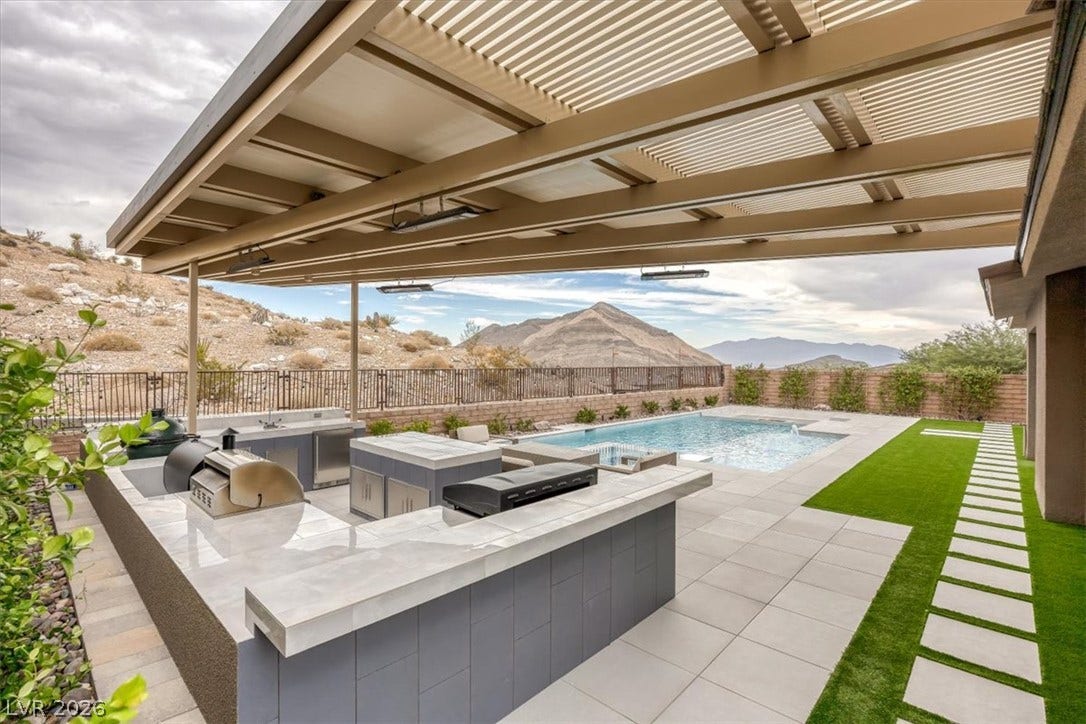 2611 Nevada Agave Lane, Las Vegas, NV 89138 An outdoor kitchen sheltered by a louvered patio cover overlooks the pool and mountain backdrop.