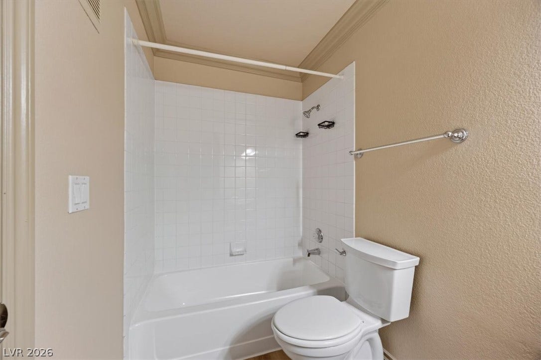 Classical crown molding accents the ceiling above a tiled tub surround and clean-lined fixtures.