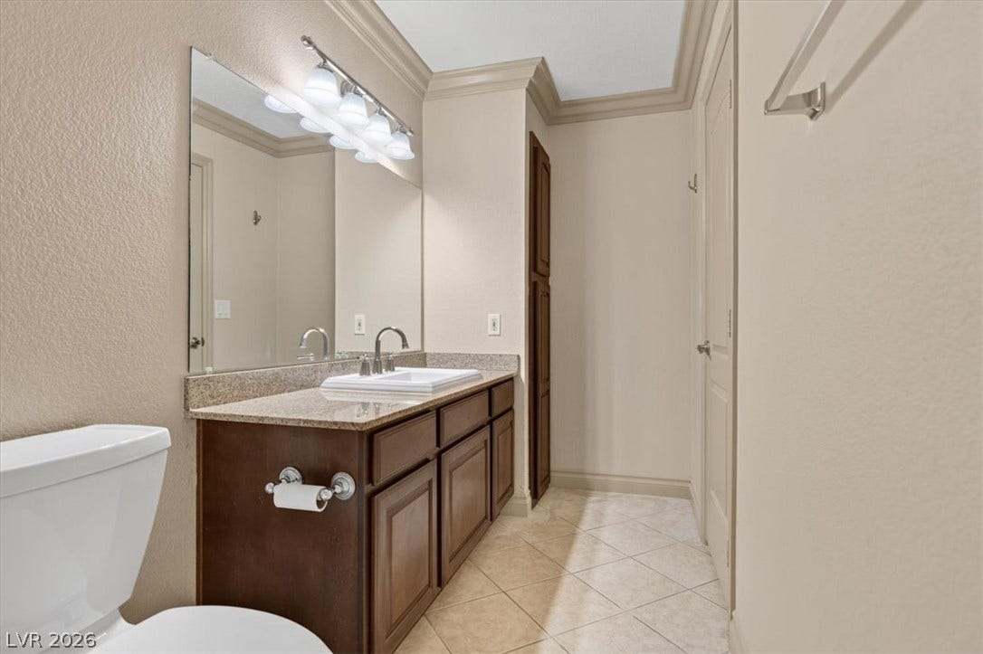 A well-appointed bathroom featuring elegant crown molding, tile flooring, and stone counters.