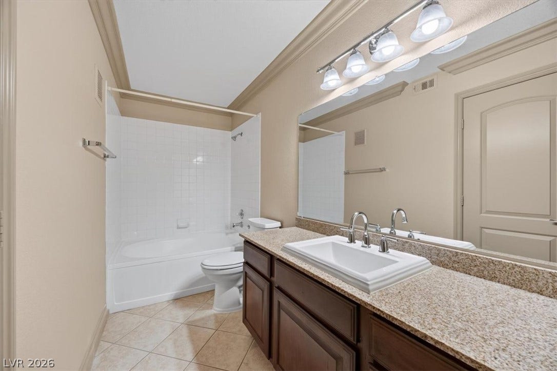 Crown molding highlights the ceiling of this functional bathroom equipped with stone counters and tile flooring.