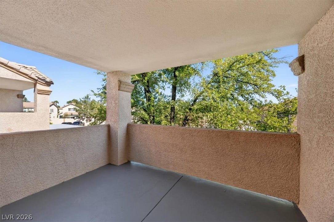 A private covered balcony overlooks mature leafy trees and the neighborhood.