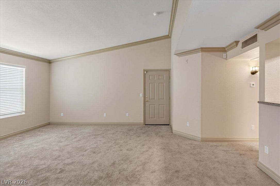 Crown molding and vaulted ceilings elevate this open living area with wall-to-wall carpeting.