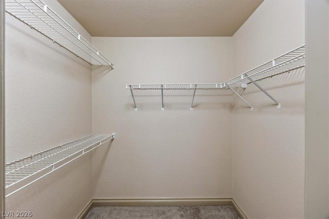 A spacious walk-in closet features built-in wire shelving and neutral carpeting.