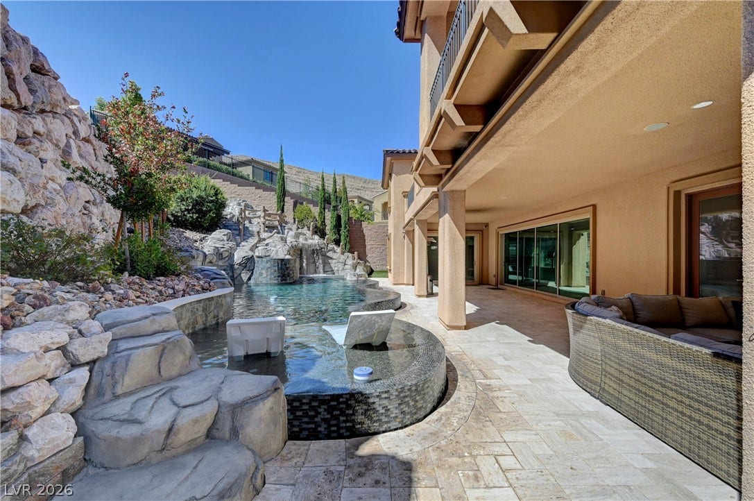 89 Olympia Chase Drive, Las Vegas, NV 89141 A spacious covered patio overlooks a custom pool featuring a built-in water slide and stone waterfall.