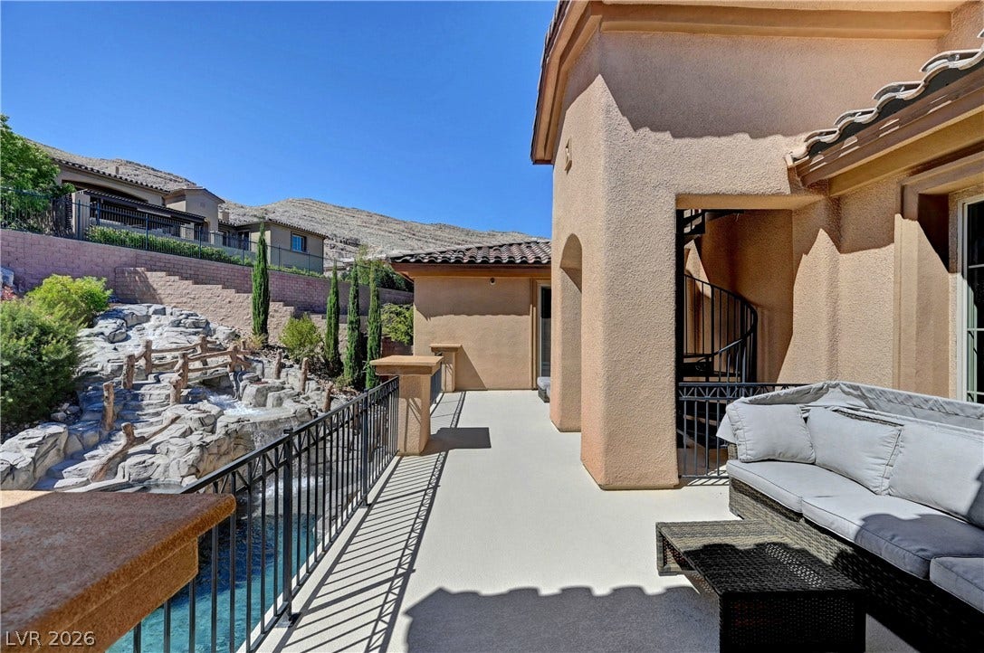 89 Olympia Chase Drive, Las Vegas, NV 89141 An elevated stone patio overlooks a rock waterfall pool set against scenic desert hills.