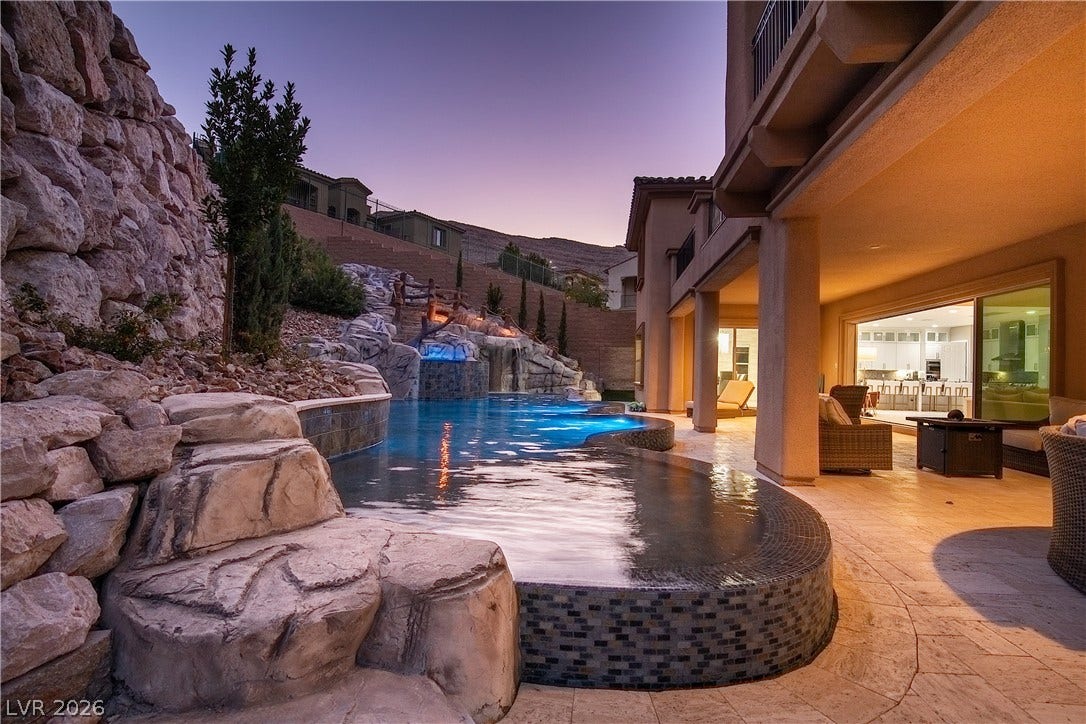 89 Olympia Chase Drive, Las Vegas, NV 89141 A custom rock waterfall flows into the tiled pool alongside a covered stone patio.