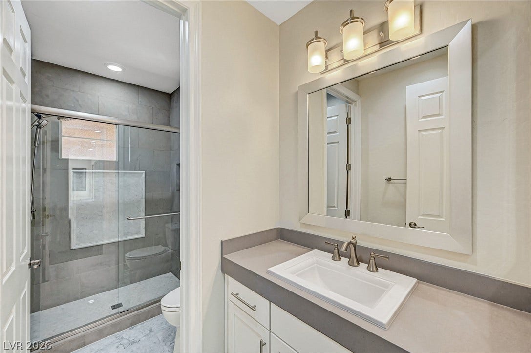 89 Olympia Chase Drive, Las Vegas, NV 89141 Smooth solid surface countertops and a glass-enclosed walk-in shower elevate this updated bathroom design.
