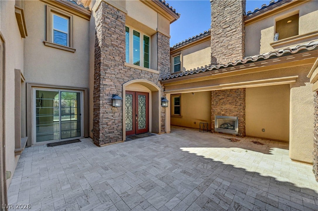 89 Olympia Chase Drive, Las Vegas, NV 89141 An inviting stone-accented courtyard featuring a cozy outdoor fireplace and elegant paver flooring.