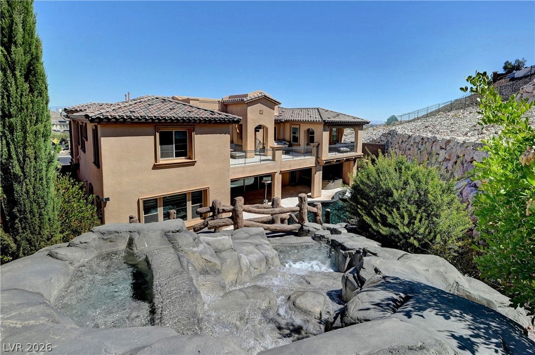 89 Olympia Chase Drive, Las Vegas, NV 89141 A stone waterfall cascades toward a multi-level Mediterranean estate featuring stucco walls and tile roofing.