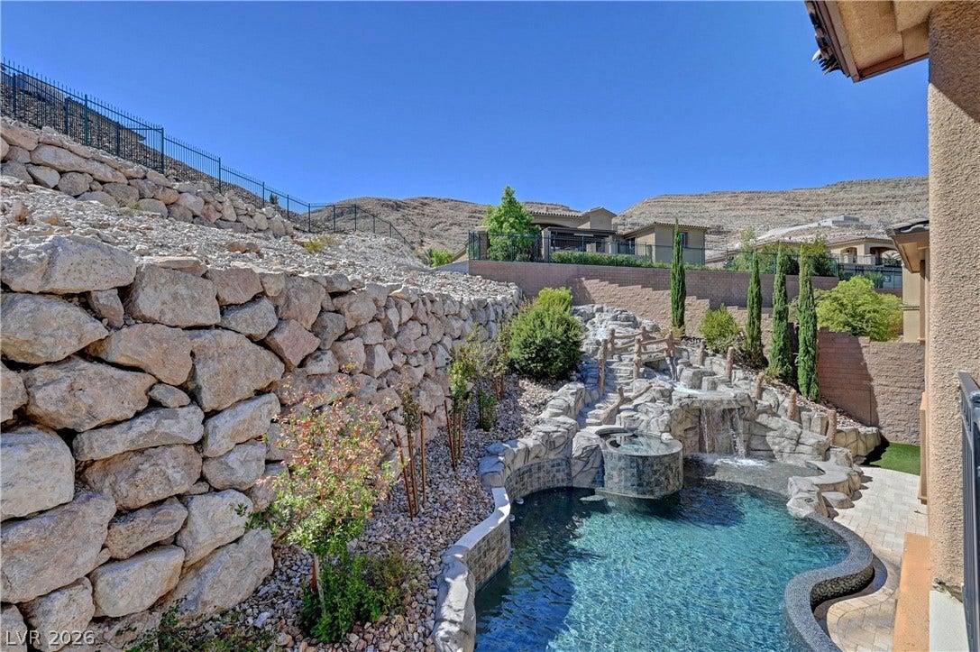 89 Olympia Chase Drive, Las Vegas, NV 89141 An inviting backyard oasis features a custom rock waterfall pool set against a tiered stone hillside.