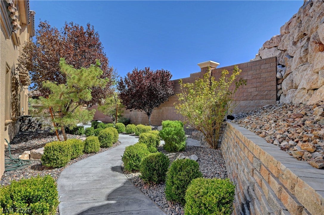 89 Olympia Chase Drive, Las Vegas, NV 89141 A curved concrete path winds through landscaped grounds flanked by stone retaining walls.