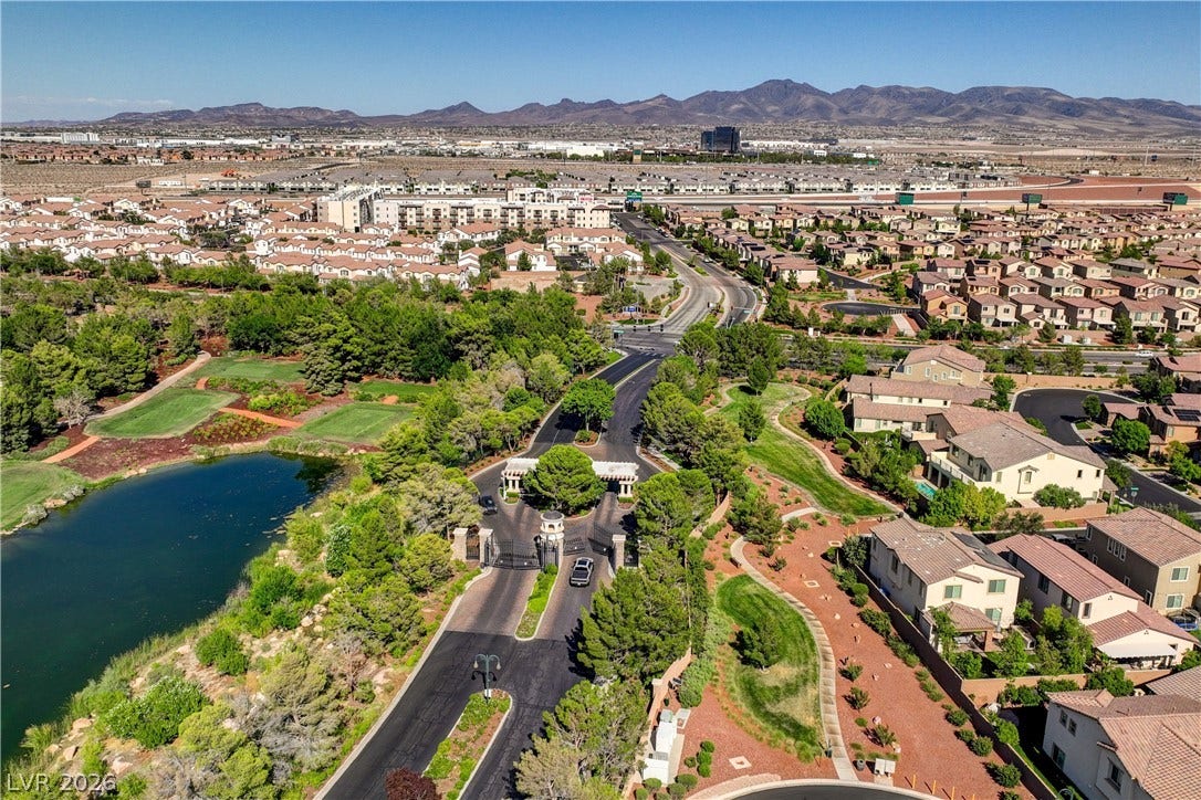 89 Olympia Chase Drive, Las Vegas, NV 89141 A gated community entrance unfolds alongside a serene pond against a mountainous desert backdrop.