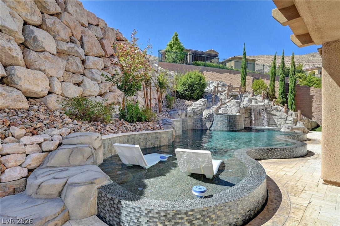 89 Olympia Chase Drive, Las Vegas, NV 89141 A natural stone retaining wall stands beside a custom swimming pool with built-in waterfall features.