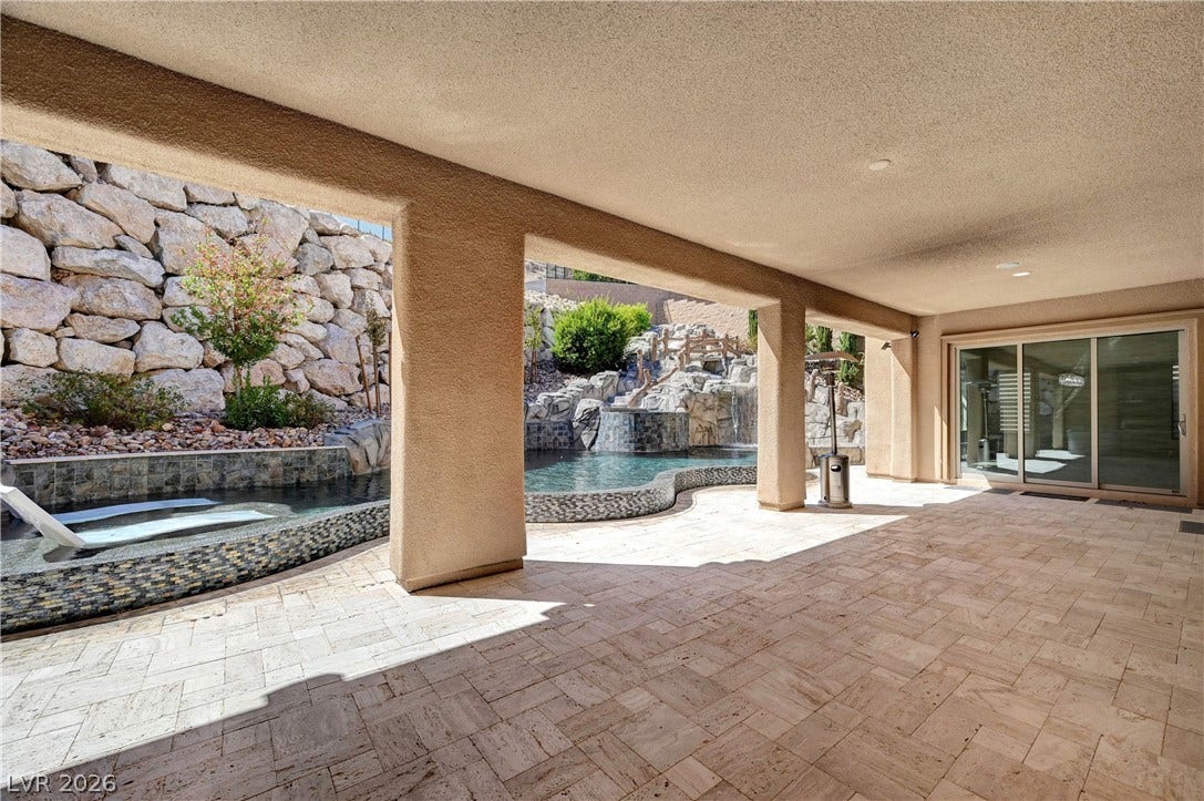 89 Olympia Chase Drive, Las Vegas, NV 89141 Shaded stone tiling extends seamlessly toward the sparkling backyard pool and rock waterfall.
