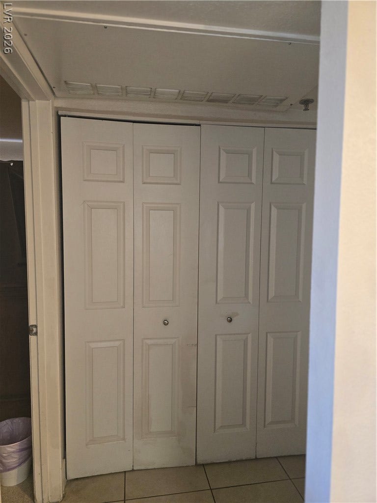 A spacious closet is concealed behind multi-panel doors situated adjacent to tiled flooring.