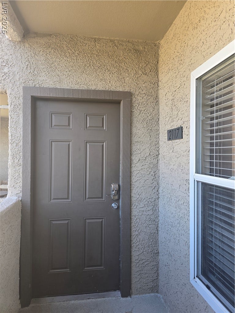 A secure, textured stucco entryway features a solid door with an electronic smart lock.