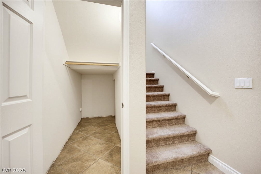 A carpeted staircase ascends next to a tiled under-stairs storage closet.