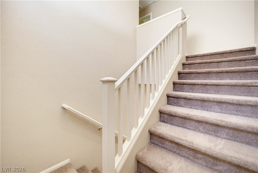 Carpeted stairs ascend alongside a classic white-painted banister under a high ceiling.