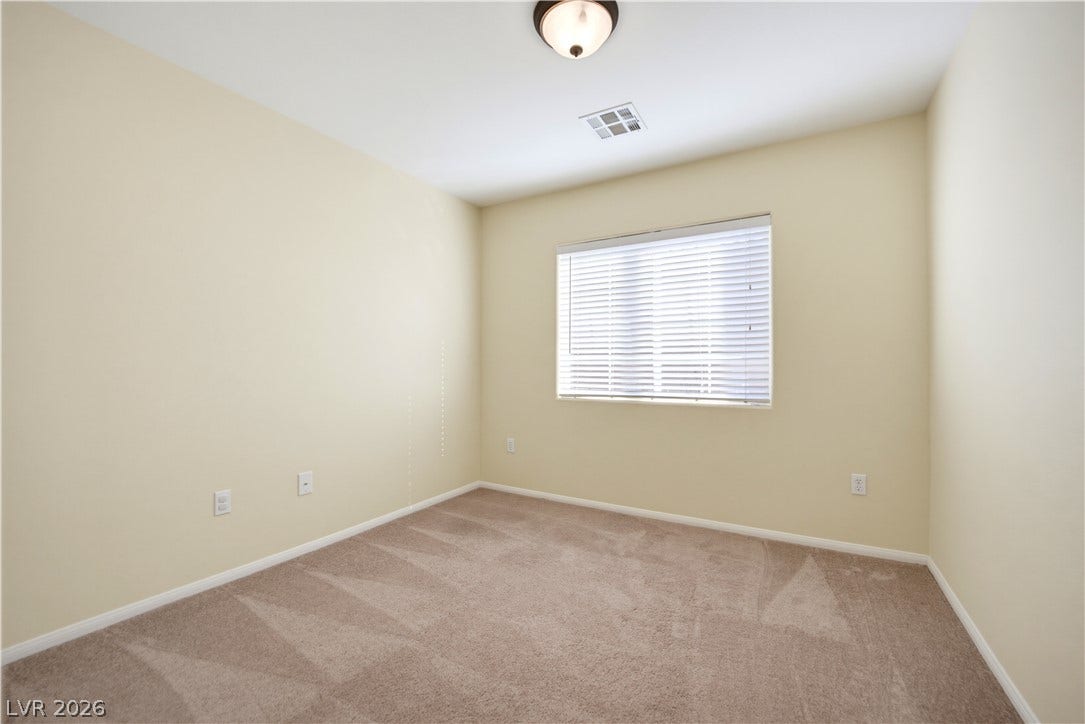 Soft carpeting pairs with neutral walls and a wide window in this versatile bedroom.