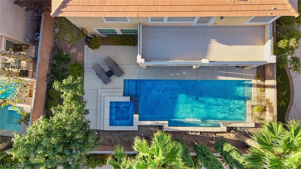 An aerial perspective showcases a sparkling swimming pool, integrated spa, and paved concrete patio area.