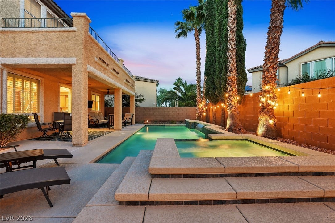 An inviting swimming pool and spa accompany the covered patio and mature palm trees.
