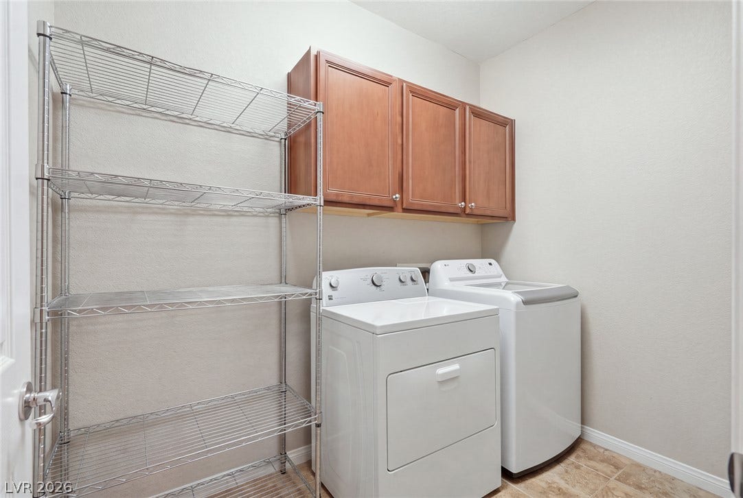 Functional laundry space features overhead wood cabinetry and tile flooring.