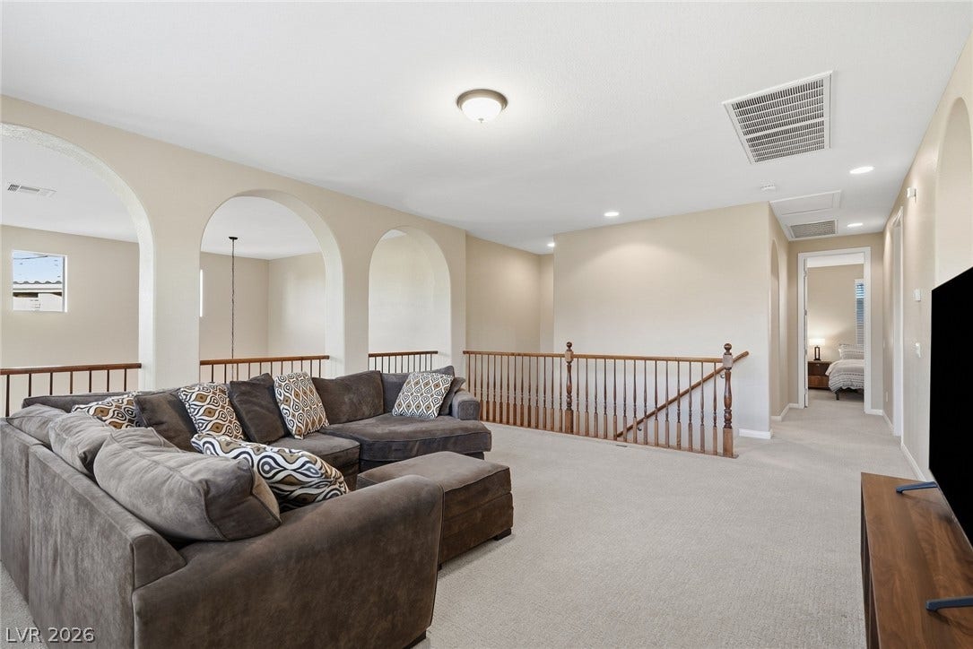 Arched architectural openings frame this versatile upper level loft featuring neutral carpeting throughout.