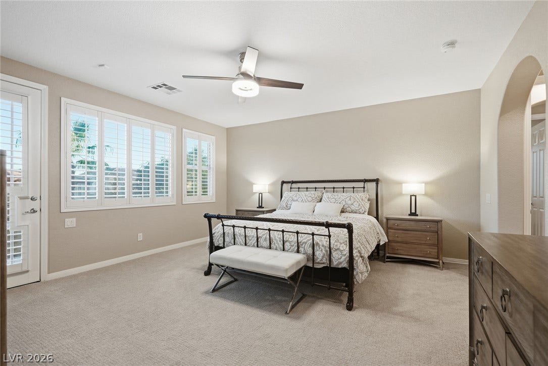 An arched doorway leads into this serene bedroom featuring plush carpeting and plantation shutters.