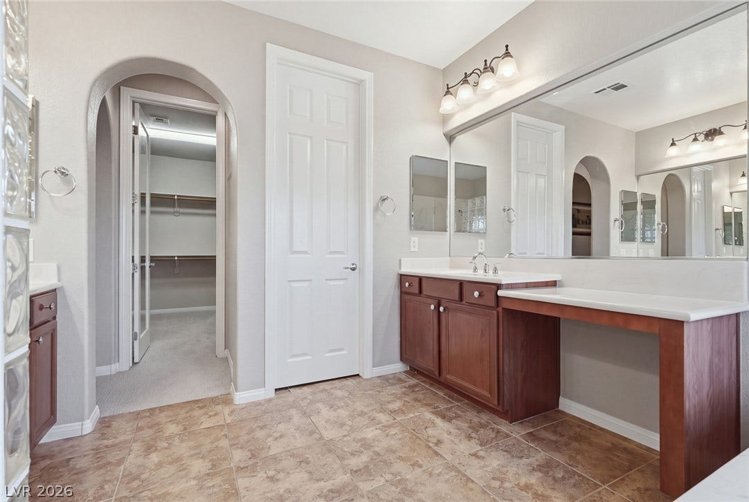 An arched doorway leads to the closet from this spacious bathroom with tile flooring.