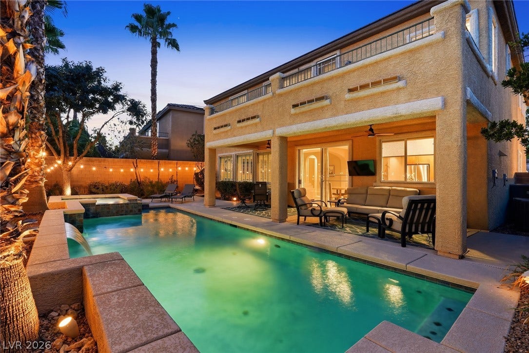 An inviting backyard oasis features a glowing swimming pool alongside a spacious covered patio.