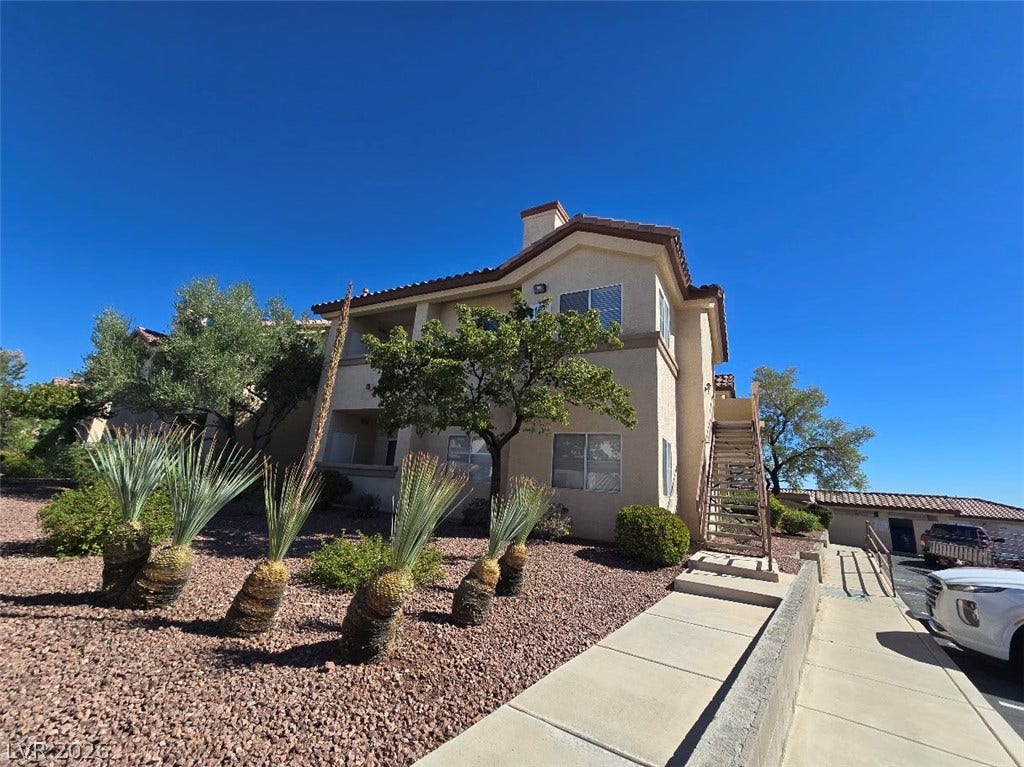 Desert plantings frame a multi-level stucco exterior with tile rooflines under a clear blue sky.