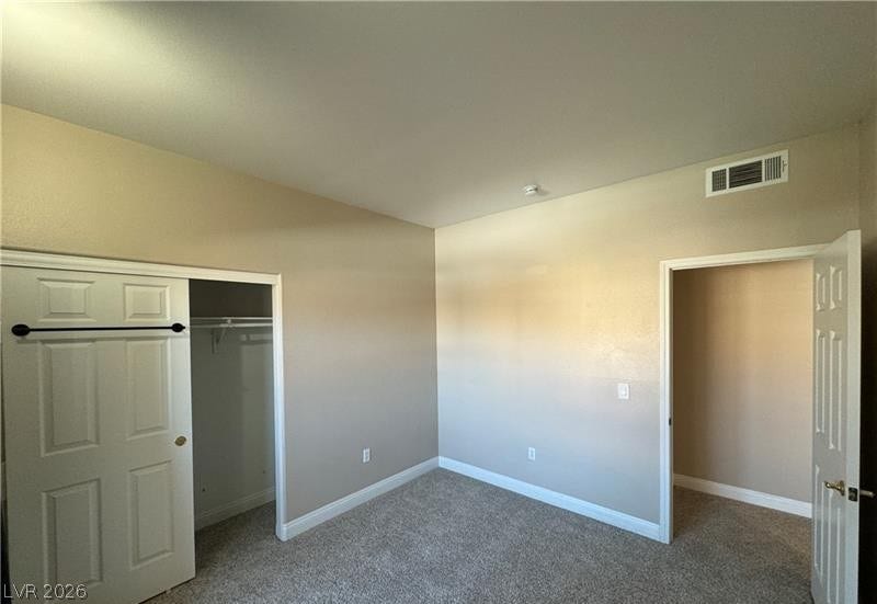A spacious bedroom features neutral walls, plush carpeting, and a walk-in closet.