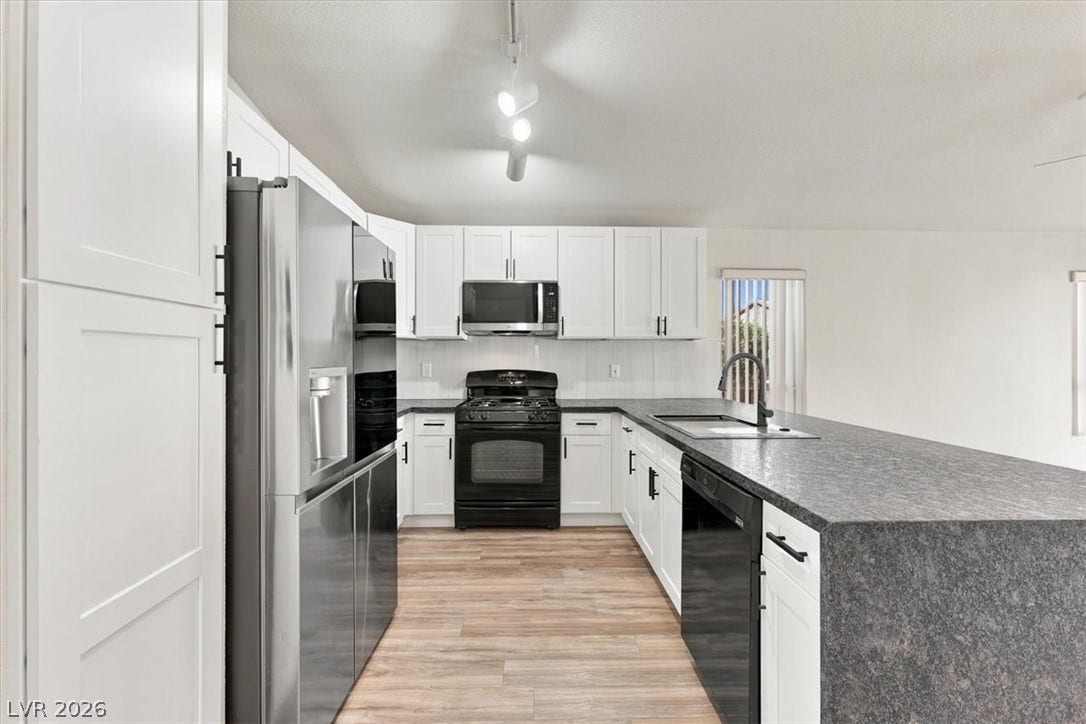 Waterfall counters with designer backsplash and white soft-close cabinetry define this open kitchen space with wood-look flooring.